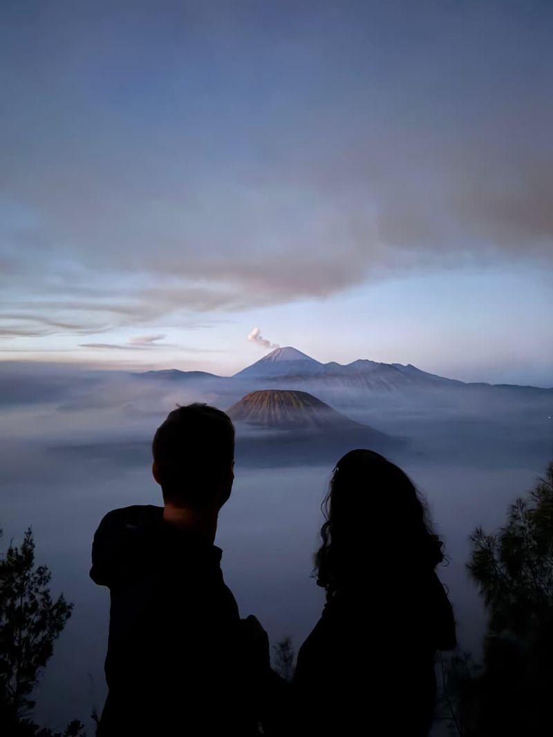 Two silhouettes looking at Mount Bromo above the clouds